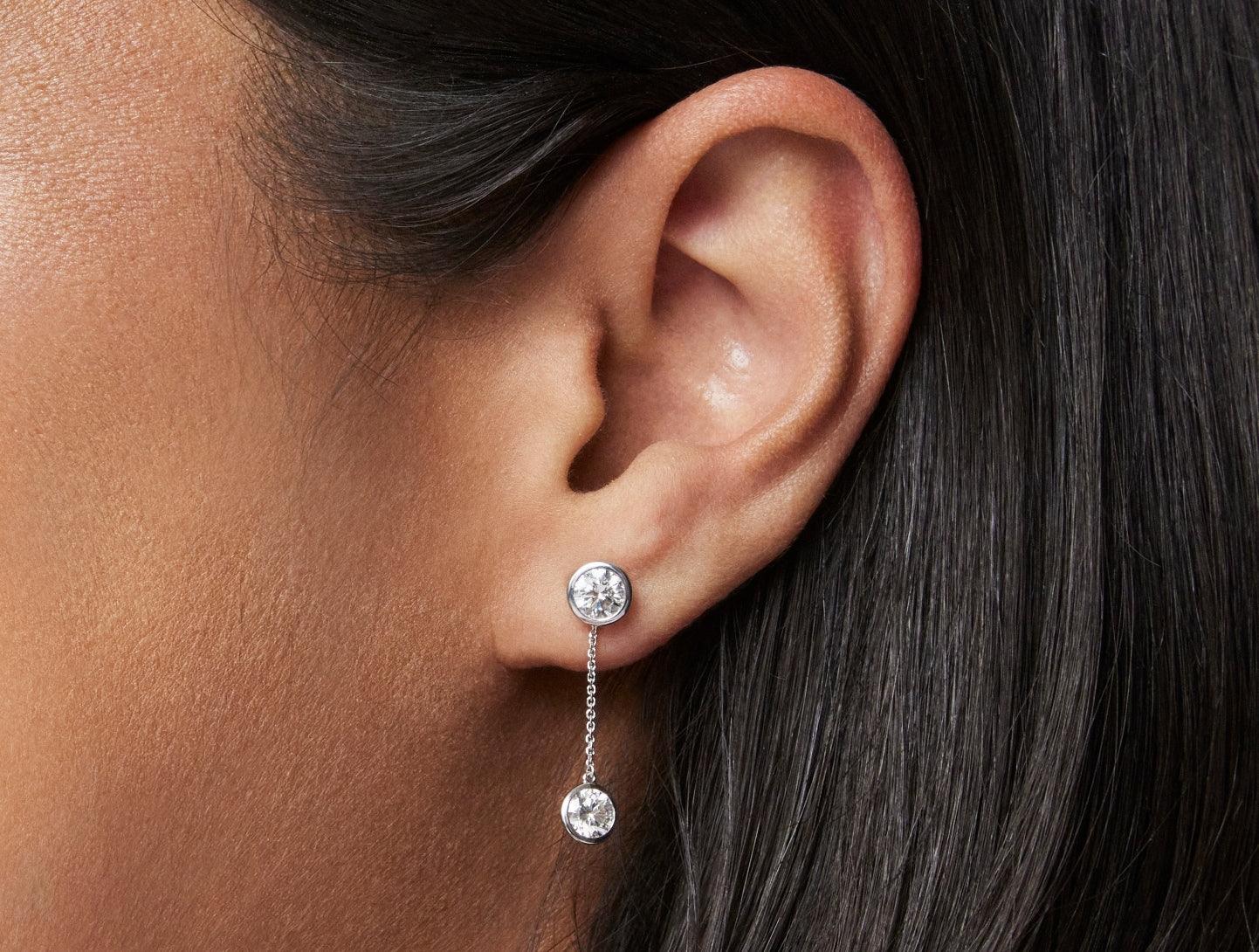 Close up model shot of 1 carat total weight round brilliant drop bezel earring jacket in 14k white gold with a 0.5 carat bezel round brilliant stud