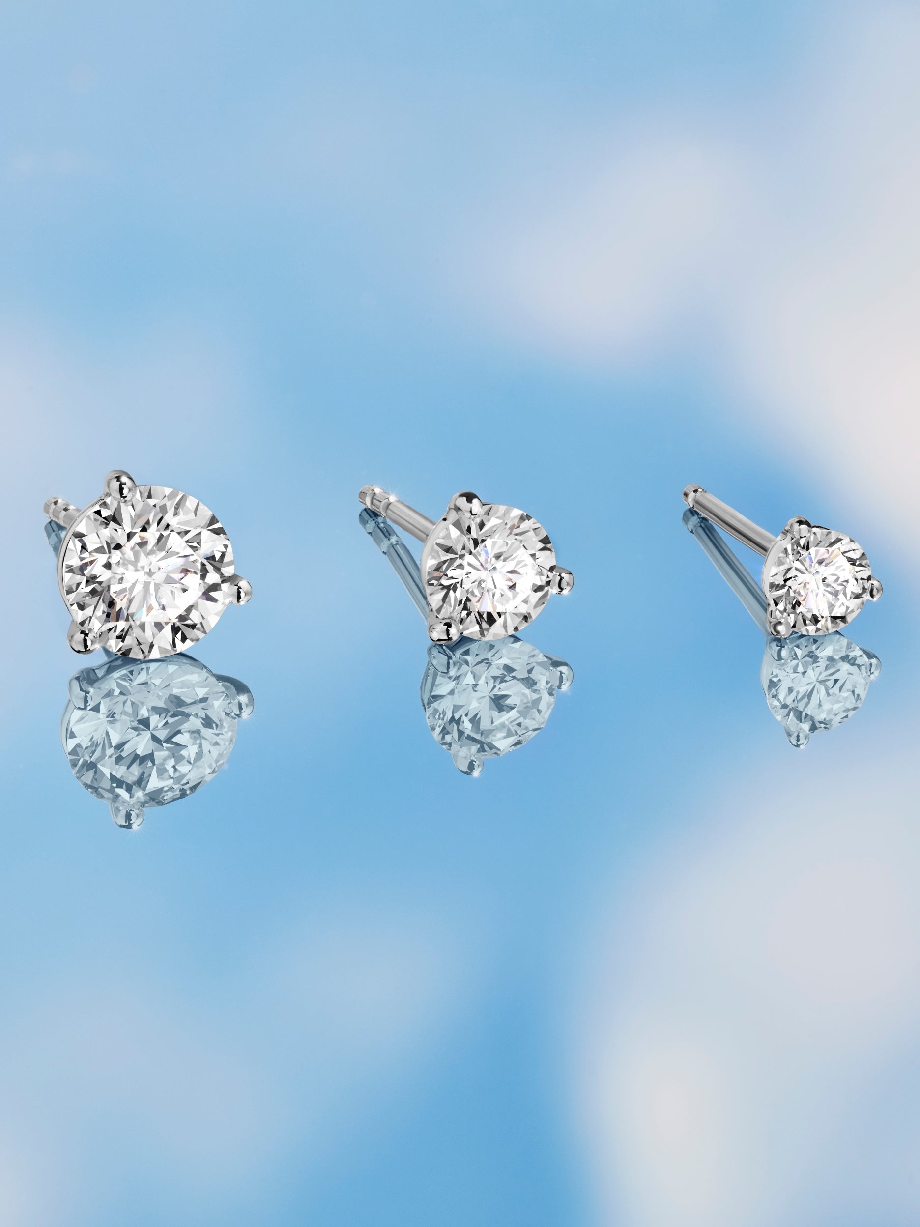 Three white round brilliant lab-grown diamond studs in decreasing carat sizes