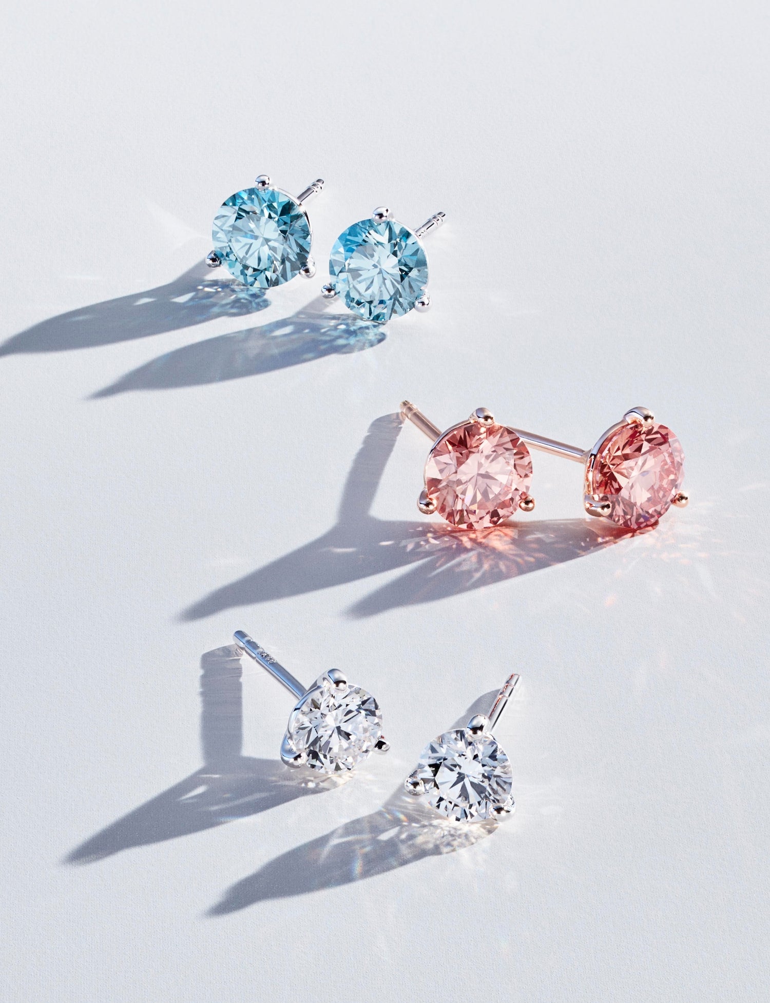 Three pairs of lab-grown diamond round brilliant studs in blue, pink and white