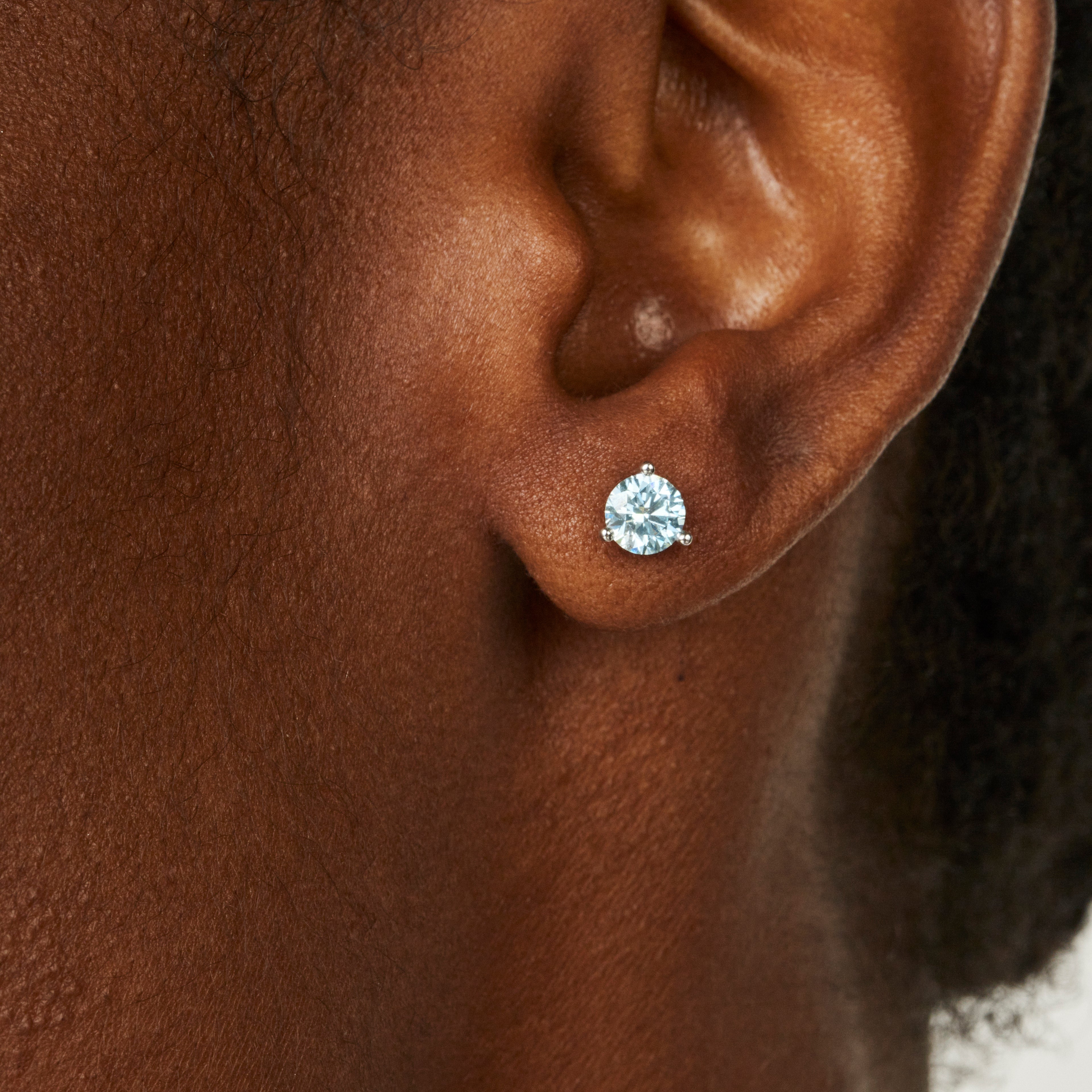 Close up on model view of blue round brilliant 1 carat diamond studs in white gold 